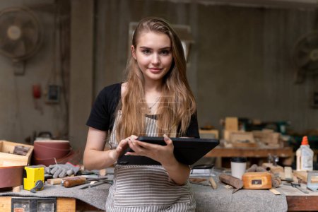 Photo for Portrait of a female carpenter looking at designs on a tablet for making her furniture in a furniture factory. with many tools and wood - Royalty Free Image