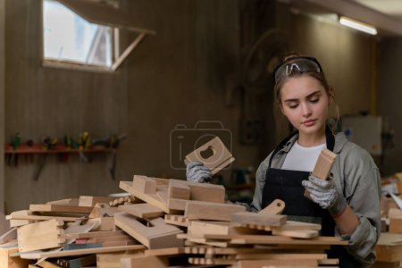 Téléchargez les photos : Une belle femme charpentier est debout pour choisir un morceau de bois à utiliser dans sa création. - en image libre de droit