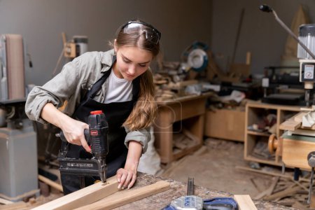 Foto de Retrato de una mujer carpintera usando herramientas para hacer muebles en una fábrica de muebles. con herramientas modernas - Imagen libre de derechos