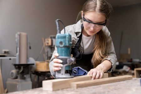 Téléchargez les photos : Portrait d'une menuisière utilisant des outils pour fabriquer des meubles dans une usine de meubles. avec des outils modernes - en image libre de droit