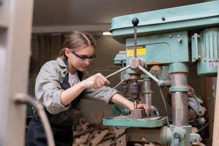 Foto de Retrato de una mujer carpintera utilizando herramientas o máquinas para cortar, no taladrar, madera para hacer muebles en una fábrica de muebles. con herramientas modernas - Imagen libre de derechos