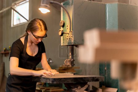 Foto de Retrato de una mujer carpintera utilizando herramientas o máquinas para cortar, no taladrar, madera para hacer muebles en una fábrica de muebles. con herramientas modernas - Imagen libre de derechos