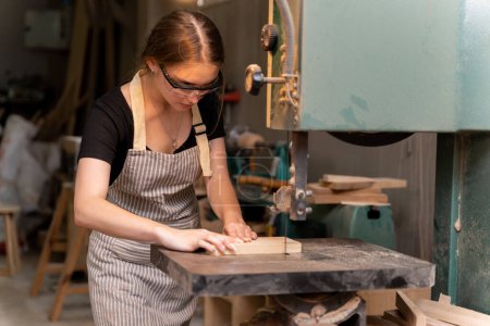 Téléchargez les photos : Portrait d'une menuisière utilisant des outils ou des machines pour couper, et non percer, du bois pour fabriquer des meubles dans une usine de meubles. avec des outils modernes - en image libre de droit