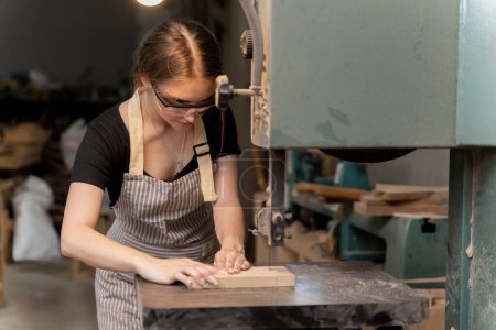 Téléchargez les photos : Portrait d'une menuisière utilisant des outils ou des machines pour couper, et non percer, du bois pour fabriquer des meubles dans une usine de meubles. avec des outils modernes - en image libre de droit