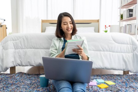Téléchargez les photos : Asian woman working at bedside in bedroom at home with her tablet - en image libre de droit
