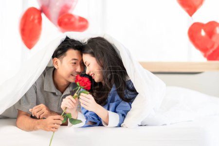Foto de Asian couple Showing love surprise giving flowers or gifts to each other on important occasions such Valentine's Day birthdays or wedding anniversaries with love and warmth in bedroom of their home - Imagen libre de derechos