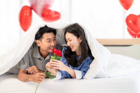 Téléchargez les photos : Asian couple Showing love surprise giving flowers or gifts to each other on important occasions such Valentine's Day birthdays or wedding anniversaries with love and warmth in bedroom of their home - en image libre de droit