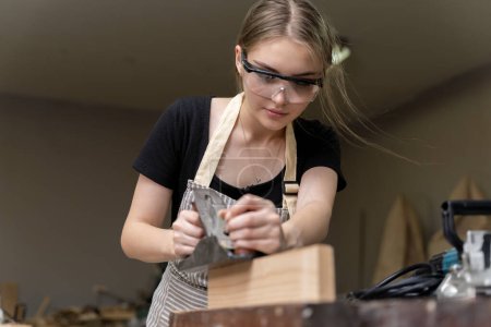 Photo for Portrait of a female carpenter using furniture tools in a furniture factory. she is using a planer planing with wood used to create furniture with modern tools - Royalty Free Image