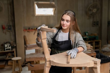 Téléchargez les photos : Une menuisière assemblant une chaise qu'elle avait conçue et construite. À l'usine de meubles trouvée dans sa maison - en image libre de droit