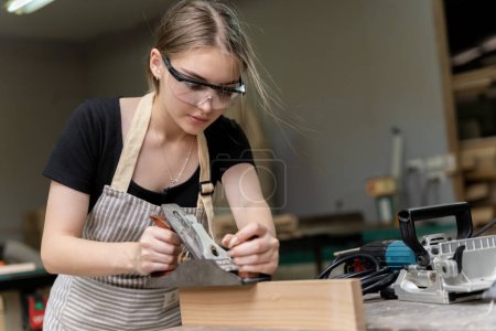 Foto de Retrato de una mujer carpintera usando herramientas de muebles en una fábrica de muebles. está utilizando una cepilladora cepilladora con madera utilizada para crear muebles con herramientas modernas - Imagen libre de derechos