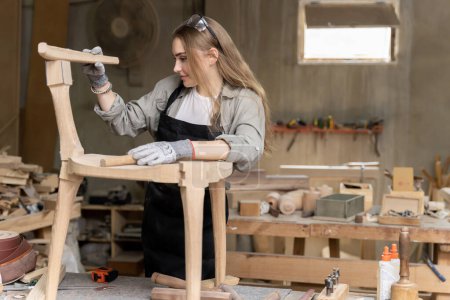Foto de Una carpintera montando una silla que había diseñado y construido. En la fábrica de muebles encontrada dentro de su casa - Imagen libre de derechos