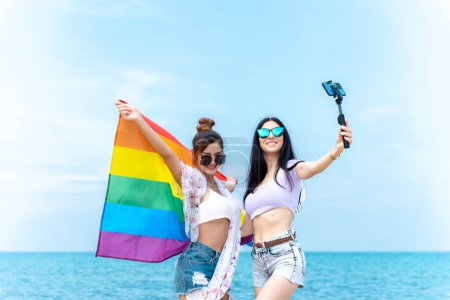 Photo for Lesbian couple with LGBTQ flags on the beach, happy couple on vacation together at sea - Royalty Free Image
