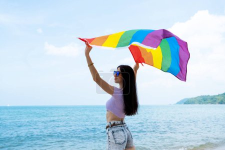 Foto de Mujer lesbiana con bandera LGBTQ en la playa, muestra su simpatía u homosexualidad - Imagen libre de derechos