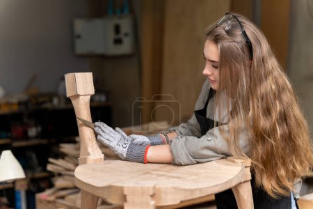 Téléchargez les photos : Une menuisière assemblant une chaise qu'elle avait conçue et construite. À l'usine de meubles trouvée dans sa maison - en image libre de droit