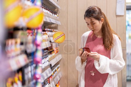 Photo for An Asian woman who is four months pregnant. Choosing food meticulously in the supermarket - Royalty Free Image