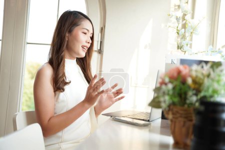 Photo for Asian woman with curly hair is working chatting with clients or colleagues via communication channels, telephone, internet with her laptop and mobile phone. - Royalty Free Image