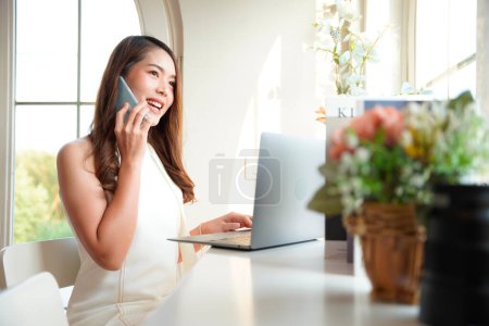Photo for Asian woman with curly hair is working chatting with clients or colleagues via communication channels, telephone, internet with her laptop and mobile phone. - Royalty Free Image