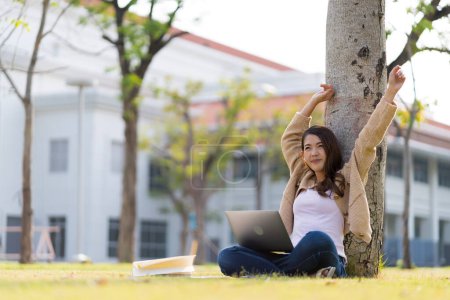 Téléchargez les photos : Étudiante asiatique Étudier pour les examens dans le domaine de l'université. Communiquer par téléphone portable ou ordinateur portable connecté à Internet. avec de nombreuses sources de connaissances - en image libre de droit