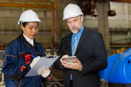 Photo for A business man inspects the work of an on-site worker at an old factory for rehearsing train engines. - Royalty Free Image