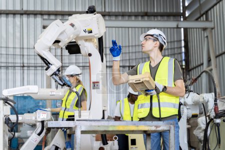 Foto de Un equipo de ingenieros masculinos y femeninos se reúnen para inspeccionar robots de soldadura de acero controlados por computadora. Plan de ensayos e instalación para su uso. - Imagen libre de derechos