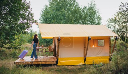 Woman traveler with luggage moving towards bedroom of cozy glamping house. Luxury camping tent for outdoor summer holiday and vacation. Lifestyle concept