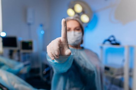 Foto de La proctóloga con uniforme médico posa mostrando los dedos y sonriendo en el hospital antes de la operación. - Imagen libre de derechos