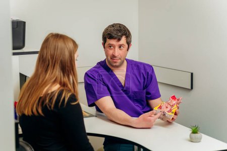Männlicher Proktologe zeigt Patientin im Krankenhaus während der Konsultation ein künstliches Modell des menschlichen Enddarms