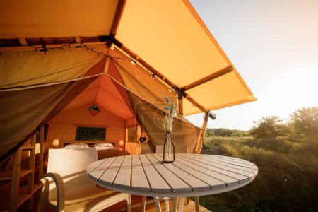 Cozy open glamping tent with light inside during sunset. Luxury camping tent for outdoor summer holiday and vacation. Lifestyle concept