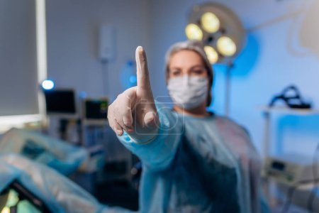 La proctóloga con uniforme médico posa mostrando los dedos y sonriendo en el hospital antes de la operación.