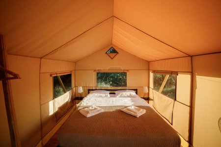 Téléchargez les photos : Intérieur de la tente glamping ouverte confortable avec lumière à l'intérieur pendant le coucher du soleil. Tente de camping de luxe pour des vacances d'été en plein air. Concept de style de vie - en image libre de droit
