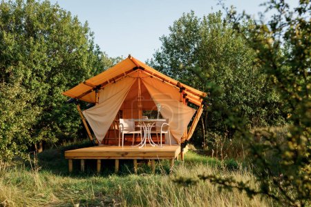 Gemütliches offenes Glamping-Zelt mit Licht im Inneren bei Sonnenuntergang. Luxus-Zeltlager für Sommerurlaub und Urlaub im Freien. Lifestyle-Konzept