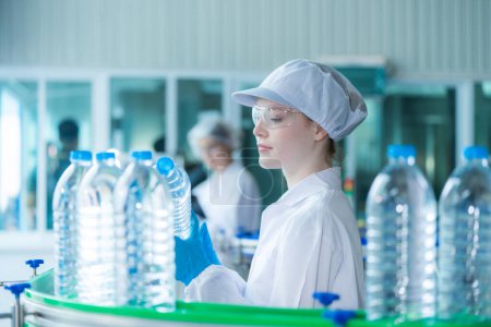 Photo for Scientist worker checking the quality of water bottles on the machine conveyor line at the industrial factory. Female worker recording data at the beverages manufacturing line production. - Royalty Free Image