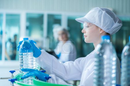 Photo for Scientist worker checking the quality of water bottles on the machine conveyor line at the industrial factory. Female worker recording data at the beverages manufacturing line production. - Royalty Free Image