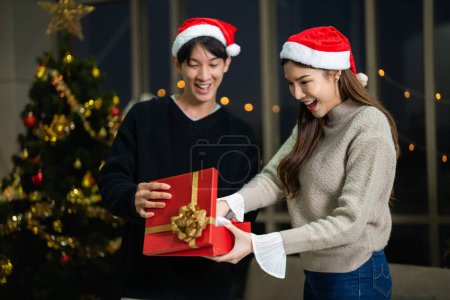 Photo for Party of beautiful asian couple female and male celebrating. happiness lovers christmas eve celebration opening box gift and present together in living room. - Royalty Free Image