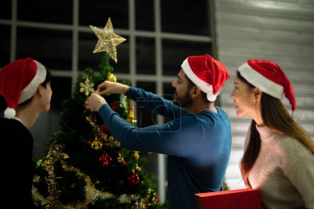 Photo for Party of friends celebrating for Christmas event and new years. men and women opening box gift and present together at home with Christmas trees. Happy loving colleague decorating Christmas tree. - Royalty Free Image
