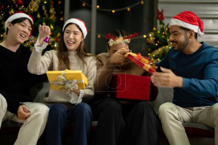 Téléchargez les photos : Groupe d'amis asiatiques profiter de la fête de Noël pour la nouvelle année célébrer. Des amis qui s'amusent à la maison. hommes et femmes ouverture cadeau boîte et cadeau ensemble à la maison avec arbre de Noël. - en image libre de droit