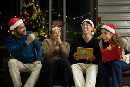 Foto de Grupo de amigos asiáticos disfrutando de la fiesta de Navidad para el año nuevo celebrar. Amigos divirtiéndose juntos en casa. regalo de la caja de apertura de hombres y mujeres y presente juntos en casa con árbol de Navidad. - Imagen libre de derechos