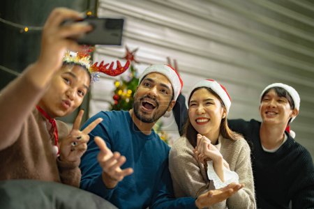 Téléchargez les photos : Fête des amis asiatiques Profiter des boissons de Noël et célébrer avoir selfie par smartphone. bonheur femmes et homme réveillon de Noël célébrer le dîner avec de la nourriture et des boissons. - en image libre de droit