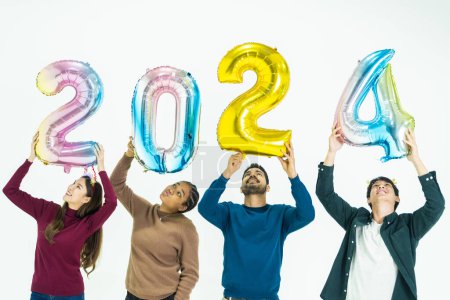 Foto de Grupo de personas que sostienen globos de colores de fantasía burbuja del número 2024 para el nuevo año. hombres y mujeres de pie sobre un fondo blanco. celebración de la fiesta feliz año nuevo - Imagen libre de derechos