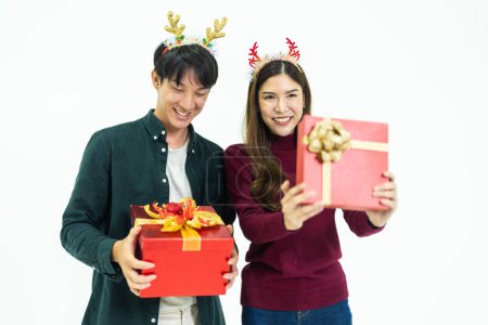Foto de Joven pareja asiática dos amigos hombre mujer vistiendo ropa casual y sosteniendo presente caja roja con regalos juntos aislados en retrato de estudio de fondo blanco. concepto de año nuevo y regalos de Navidad. - Imagen libre de derechos