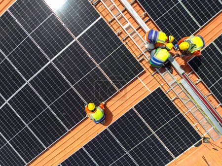 Téléchargez les photos : Aérienne supérieure des hommes ingénieurs inspecte la construction de panneaux solaires ou de cellules photovoltaïques sur le toit. Énergie renouvelable industrielle de l'énergie verte. usine en zone urbaine. travailleur travaillant sur le toit de la tour. - en image libre de droit