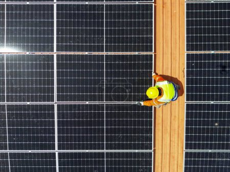Téléchargez les photos : Aérienne supérieure des hommes ingénieurs inspecte la construction de panneaux solaires ou de cellules photovoltaïques sur le toit. Énergie renouvelable industrielle de l'énergie verte. usine en zone urbaine. travailleur travaillant sur le toit de la tour. - en image libre de droit