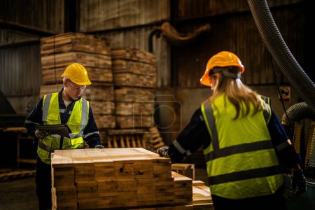 Photo for Team worker carpenter wearing safety uniform and hard hat working and checking the quality of wooden products at workshop manufacturing. man and woman workers wood in dark warehouse industry. - Royalty Free Image