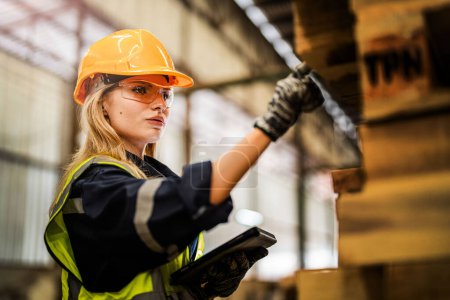 Photo for Woman worker carpenter wearing safety uniform and hard hat working and checking the quality of wooden products at workshop manufacturing. man and woman workers wood in dark warehouse industry. - Royalty Free Image