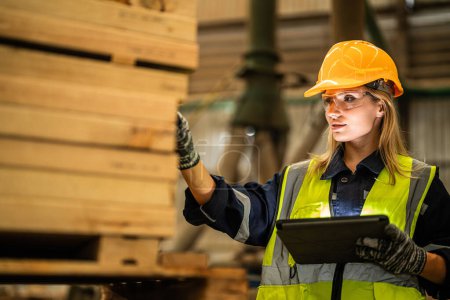 Photo for Woman worker carpenter wearing safety uniform and hard hat working and checking the quality of wooden products at workshop manufacturing. man and woman workers wood in dark warehouse industry. - Royalty Free Image