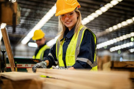 Photo for Woman cleaning timber wood in dark warehouse industry. Team worker carpenter wearing safety uniform and hard hat working and checking the quality of wooden products at workshop manufacturing. - Royalty Free Image