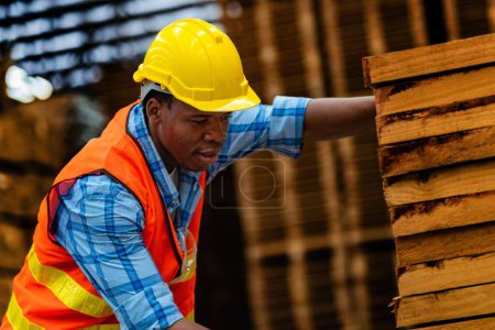Photo for African worker carpenter wearing safety uniform and hard hat working and checking the quality of wooden products at workshop manufacturing. man and woman workers wood in dark warehouse industry. - Royalty Free Image