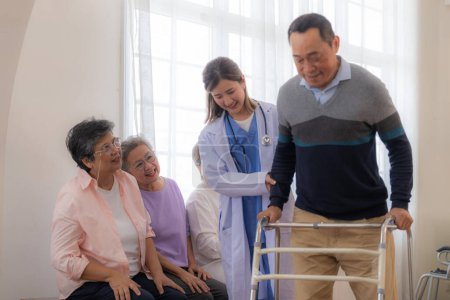 Photo for Asian young nurse support senior older man walk with walker. Beautiful nurse help and take care. elderly mature grandpa patient doing physical therapy with a group of senior friends in hospital. - Royalty Free Image