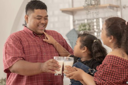 Téléchargez les photos : Une famille asiatique boit du lait. Ils étaient heureux d'inviter leur fille à boire du lait le matin ensemble dans la cuisine de leur maison. Heure du petit déjeuner de papa asiatique maman et enfant. - en image libre de droit