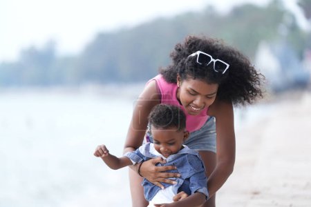 Téléchargez les photos : Mixte race africaine et asiatique mère et garçon joue à l'espace extérieur. souriant famille heureuse avoir du plaisir à courir sur la plage. portrait de maman et d'enfant style de vie avec une coiffure unique. - en image libre de droit